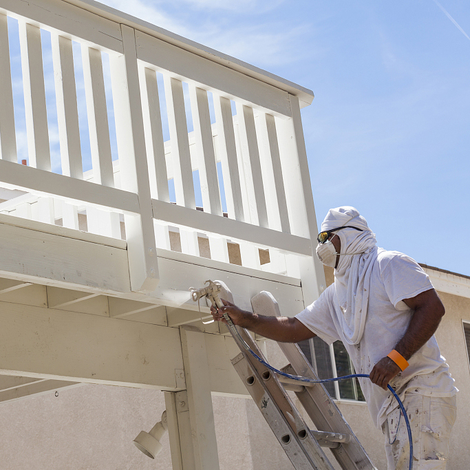 House Painter Wearing Facial Protection Spray Painting A Deck of A Home.